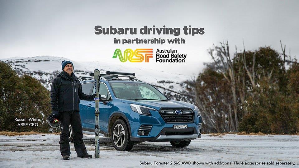 Russell White posing in front of a blue Subaru holding skis and helmet for Road Safety Foundation