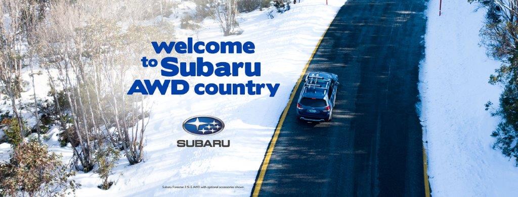 Subaru welcome banner with blue Subaru driving on the road in snowy conditions