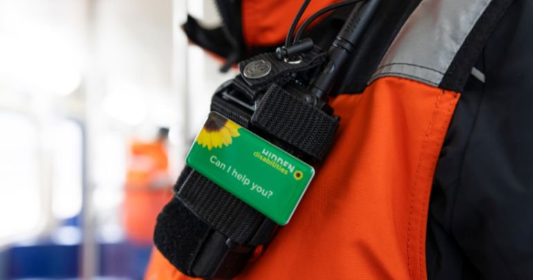 Perisher staff member and Skitube attendant assisting a young child wearing a Hidden Disabilities Sunflower lanyard on the Skitube platform