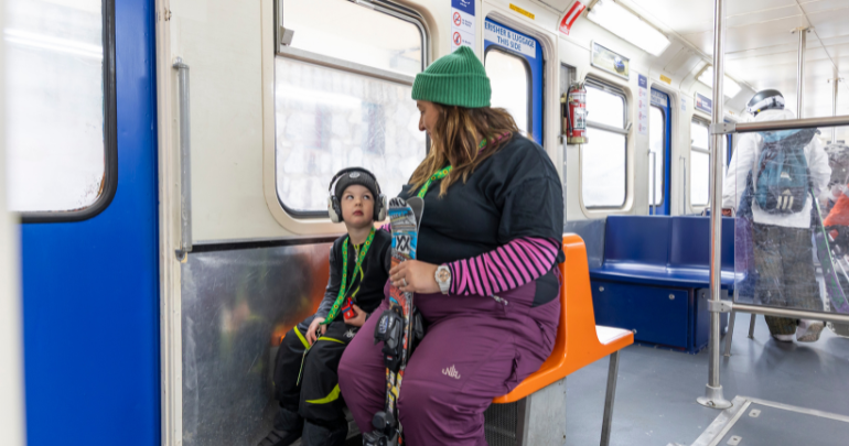 Parent and child wearing noise-cancelling headphones and a Sunflower lanyard travelling on the Skitube